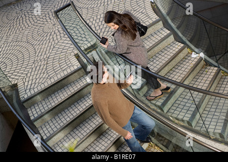Un giovane uomo e donna sono passando tra di loro su una scalinata che porta a mano i dispositivi computerizzati. Foto Stock