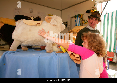 Ragazza petting un giocattolo imbottito di ram a una pelle e pellicce artigianali chiosco, settimanale dell'agricoltore nel mercato Muehldorf am Inn, superiore Ba Foto Stock