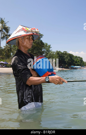 Pescatore locale in piedi in mare, tenendo in mano una canna da pesca per la cattura di pesci, Isola di Lombok, Lesser Sunda Islands, Indonesia, Asia Foto Stock