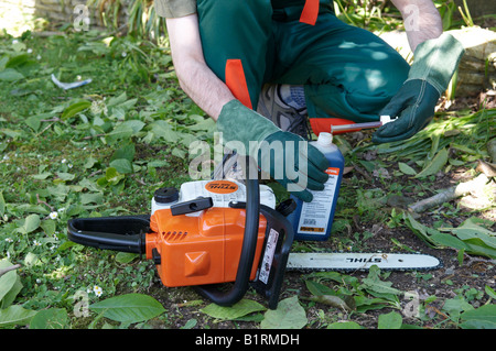 L uomo nella piena STIHL protettiva power tool di riempimento di abbigliamento la sua chainsaw MS 180 con olio della catena Foto Stock