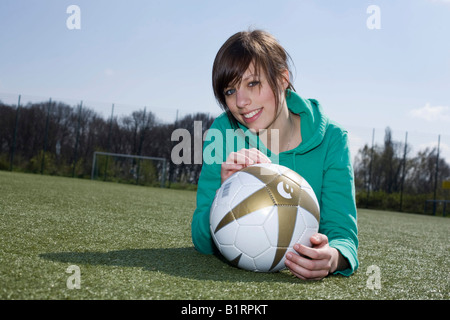 Giovane donna giaceva con un calcio di fronte a lei su un campo di calcio Foto Stock