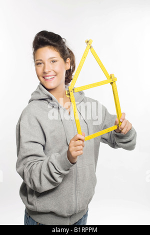 Giovane donna sorridente nella fotocamera tiene nelle sue mani un giallo righello piegato nella forma di una casa Foto Stock