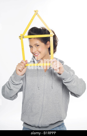 Giovane donna sorridente nella fotocamera tiene nelle sue mani un giallo righello piegato nella forma di una casa Foto Stock