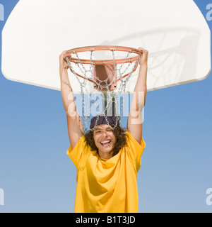 Un teenager di giocatore di basket pende da una Basketball hoop e sorrisi Foto Stock