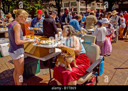 Portando il suo cane sul grembo di una sedia a rotelle legato donna si affianca ad altre persone senza dimora per una domenica senza pasto in Portland Oregon Foto Stock