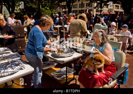 Portando il suo cane sul grembo di una sedia a rotelle legato donna si affianca ad altre persone senza dimora per una domenica senza pasto in Portland Oregon Foto Stock