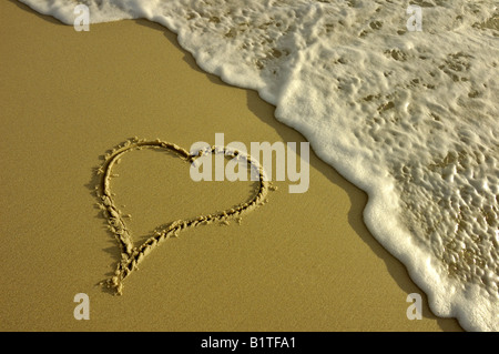 Un cuore disegnato nella sabbia in procinto di essere lavato via da un'onda. Prese in condizioni di scarsa illuminazione di sera. Foto Stock