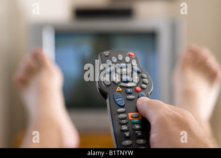 Un uomo guarda la televisione e cambia i canali durante i momenti di relax in una domenica pomeriggio Foto Stock