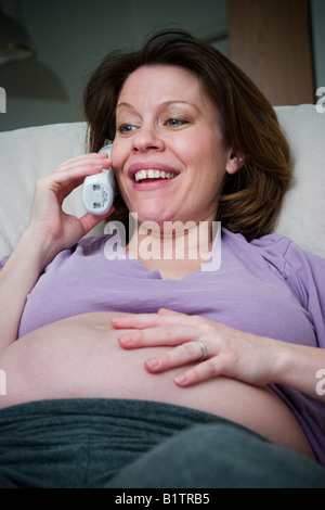 Donna incinta seduta su una sedia e parlando al telefono modello rilasciato Foto Stock