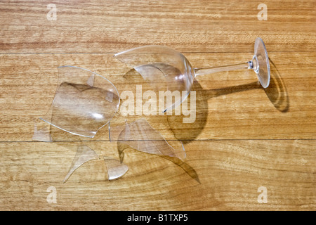 La rottura di un bicchiere di vino su un pavimento di legno con un'ombra che mostra il profilo del vetro Foto Stock