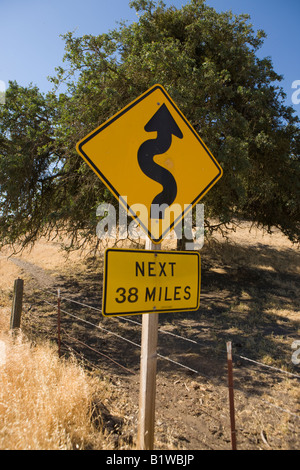Un giallo autostrada segno che indica che il prossimo 38 miglia saranno giri di avvolgimento, California, Stati Uniti d'America. Foto Stock