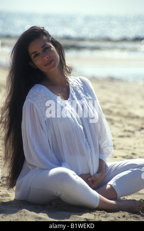 Etnia donna seduta sulla spiaggia guardando nella telecamera Foto Stock