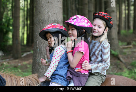 Tre amici una bionda caucasica e due asian 9 anni 5 anni sui cavalli in una foresta Foto Stock