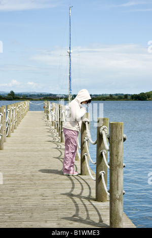 Una donna su un molo di indossare una felpa con cappuccio sguardi premurosamente nell'acqua Foto Stock