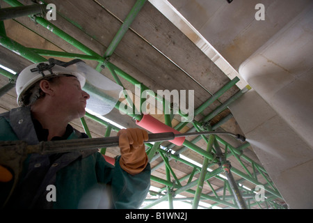 Un lavoratore utilizza acqua ad alta pressione per pulire residui dal muro di pietra. Foto Stock