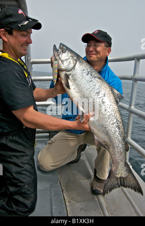 Oriental l uomo e la guida di contenimento e ammirando un grande Salmone Chinook pesce pescato su uno sport trollata cucchiaio esca artificiale Foto Stock