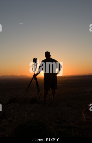 Un uomo guarda il sole che tramonta su un alta cima Foto Stock