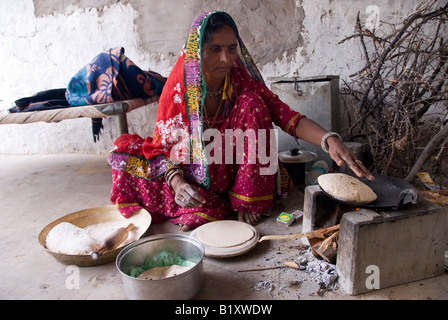 La donna da Rajasthan (India) prepara il cibo. La cottura su stufa tradizionale nel cortile della casa. Il tipico abito e navi. Foto Stock