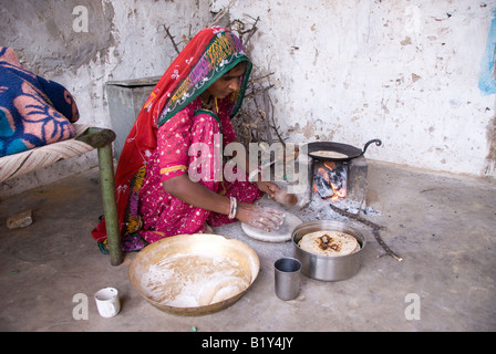 La donna da Rajasthan (India) prepara il cibo. La cottura su stufa tradizionale nel cortile della casa. Il tipico abito e navi. Foto Stock