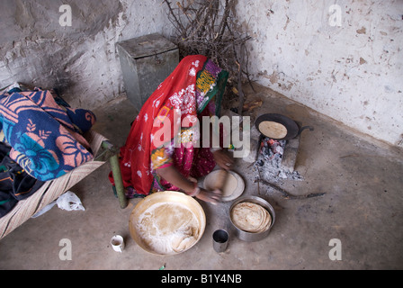 La donna da Rajasthan (India) prepara il cibo. La cottura su stufa tradizionale nel cortile della casa. Il tipico abito e navi. Foto Stock