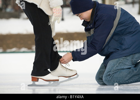 Giovane uomo legatura di pattino da ghiaccio lacci di una giovane donna Foto Stock