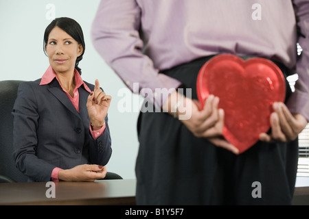 Uomo in piedi di fronte ad una imprenditrice e nascondere un cuore dono sagomato Foto Stock