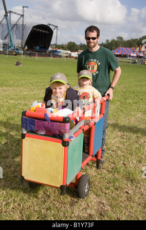 Due giovani ragazzi essendo spinto in un carrello dal loro padre presso il festival di Glastonbury 2008 Foto Stock