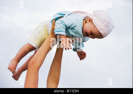 Il Toddler girl a metà in aria sollevato dai bracci di madre Foto Stock