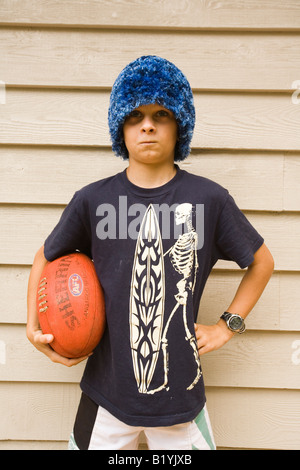 Grave ragazzo difficili con divertenti fluffy hat tenendo un pallone da rugby Foto Stock