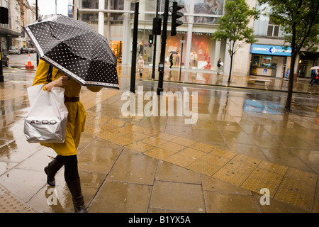 Donna cammina a Londra portando un ombrello maculato sotto la pioggia Foto Stock