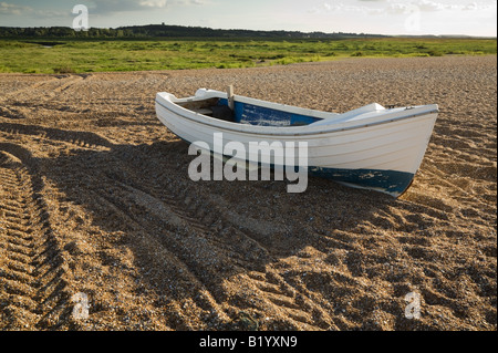 Unica piccola barca spiaggiata sulla spiaggia di ciottoli a Blakeney, Costa North Norfolk Foto Stock