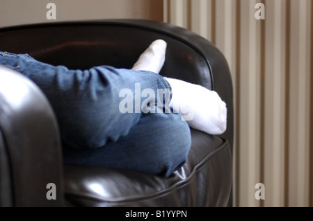 Fotografia della ragazza seduta sul divano che mostra le gambe e piedi solo cercando confortevoli nella casa di famiglia REGNO UNITO Foto Stock