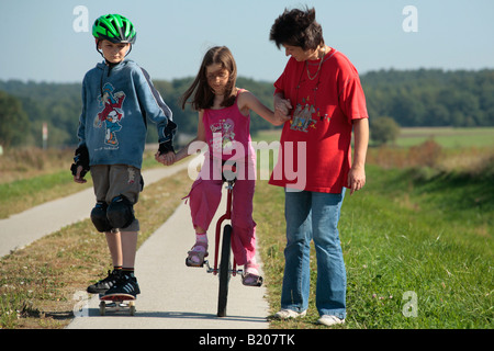 Il fratello e la madre sta aiutando una giovane ragazza di cavalcare un monociclo Foto Stock