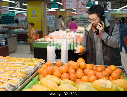 Giovane uomo cinese usando il cellulare mentre la scelta di arance in un supermercato di Chongqing Cina Foto Stock