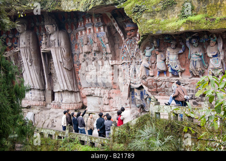 Tourist guardare Anicca dio del destino, trattenendo il volante della vita Dazu incisioni rupestri Monte Baoding in Cina Foto Stock