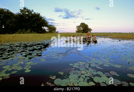 Un gruppo di turisti pongono per la telecamera su un mokoro gita in barca nel Delta dell'Okavango al tramonto. Foto Stock