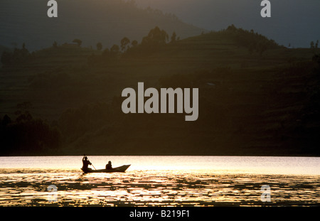 Due uomini locali in un ceppo di legno piroga paddeling sul lago Bunyonyi e in silhouette al tramonto. Foto Stock