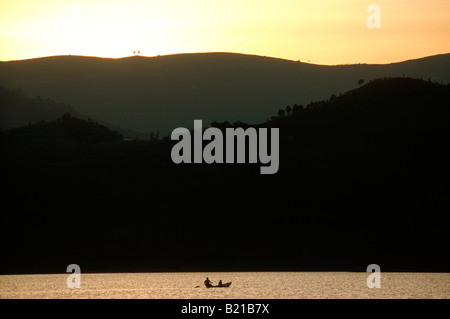 Due uomini locali in un ceppo di legno piroga paddeling sul lago Bunyonyi e in silhouette al tramonto. Foto Stock