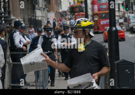 Anarchico in ciclo casco mani libere foglio notizie circa il G8 sulla strada fuori dell Ambasciata giapponese di Londra guardato dalla polizia Foto Stock