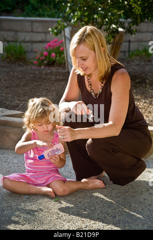 Una giovane madre si applica per la protezione solare non cooperativo sua figlia di due anni nel giardino della loro casa in California del Sud Foto Stock