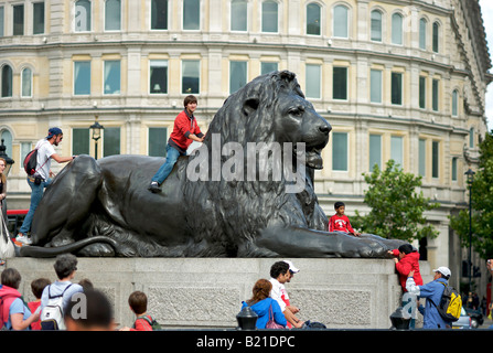 I turisti salire i leoni di bronzo al piede della colonna di Nelson in Trafalgar Square London REGNO UNITO Foto Stock