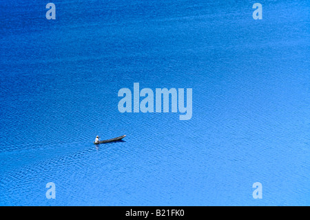 Un solitario solitario uomo locale in un ceppo di legno piroga paddeling sul lago Bunyonyi e. Foto Stock