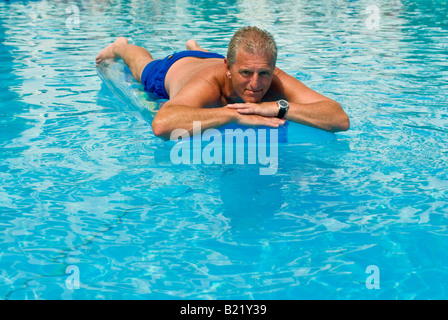 Ritratto orizzontale di un abbronzato uomo caucasico giacente su un lilo nel mezzo di un blu brillante hotel piscina Foto Stock