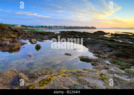 La rottura dell'alba sulla foreshore a Goodrington Sands nel South Devon con il primo bagliore di luce del sole che riflette sul mare Foto Stock