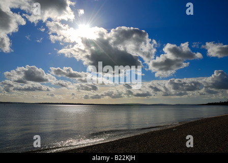 Sun attraverso le nuvole con la spiaggia e il mare in primo piano a Calshot Inghilterra Hampshire REGNO UNITO Foto Stock