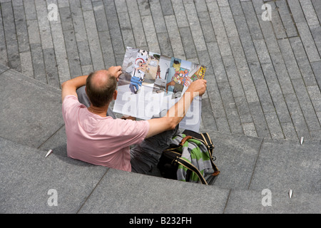 Un uomo calvo probabilmente un turista tenendo un libro guida seduta nel convogliatore al di fuori del Municipio di Londra Foto Stock