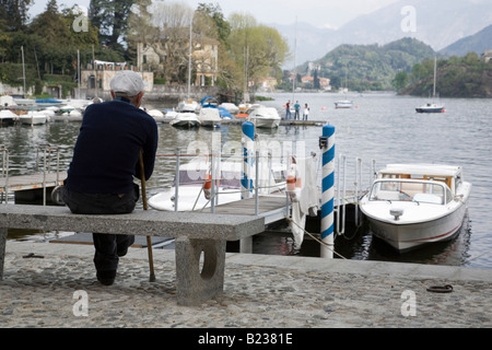 Il vecchio uomo si siede un banco di pietra nel villaggio di Sala Comacina, Lago di Como, Italia Foto Stock