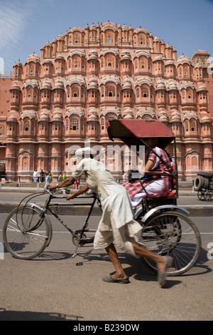 Il triciclo rickshaw driver (wallah) spinge i passeggeri lungo streeet davanti al palazzo dei venti di Jaipur India Rajasthan Foto Stock