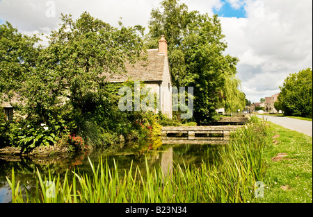 Il neonato Fiume Tamigi che fluisce oltre il case di villaggio a Ashton Keynes, Wiltshire, Inghilterra, Regno Unito Foto Stock