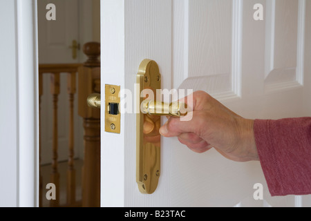 Donna che apre o chiude una porta di legno bianco girando maniglia con la mano su chiusura d'oro al piano superiore stanza. Inghilterra Gran Bretagna Foto Stock